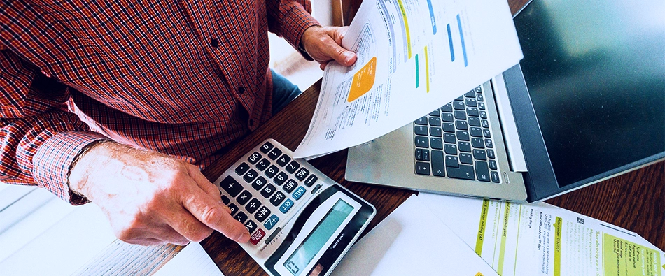 Imagem mostra uma pessoa com conta e uma calculadora na mão analisando se vai fazer um empréstimo para quitar dívidas.
